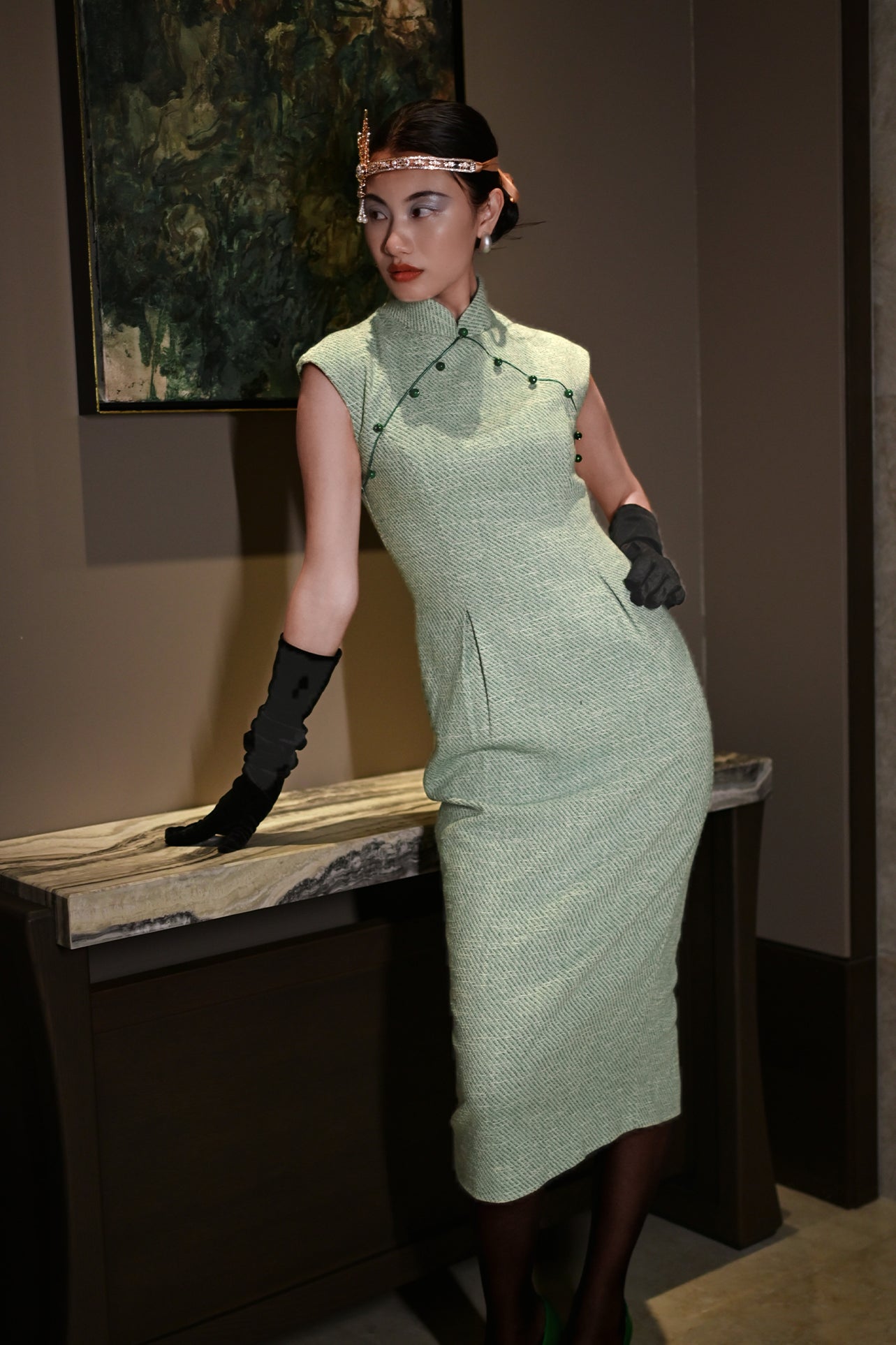 A stylish woman wearing sunglasses and holding a black folding fan, dressed in an elegant mint green sleeveless modern qipao dress featuring a mandarin collar with delicate button trim along the bodice and a tailored midi sheath silhouette.