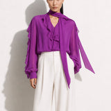 A style comparison of two professional corporate outfits featuring long-sleeve ruffled chiffon blouses with versatile tie-neck scarves; the left styled in purple with white wide-leg trousers, and the right in grey paired with a mustard yellow high-waisted pencil skirt.