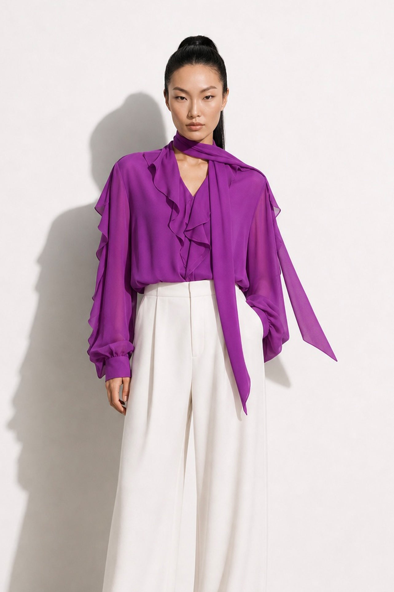 A style comparison of two professional corporate outfits featuring long-sleeve ruffled chiffon blouses with versatile tie-neck scarves; the left styled in purple with white wide-leg trousers, and the right in grey paired with a mustard yellow high-waisted pencil skirt.