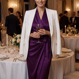 A professional woman modeling an elegant deep purple satin wrap midi dress, featuring a sophisticated surplice V-neck, cap sleeves, and a chic side bow tie for a quiet luxury evening or office look.