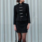 A detailed shot of a woman modeling a sophisticated black woven tweed mini skirt adorned with subtle shimmering crystals, tailored in a sleek high-waisted pencil cut.