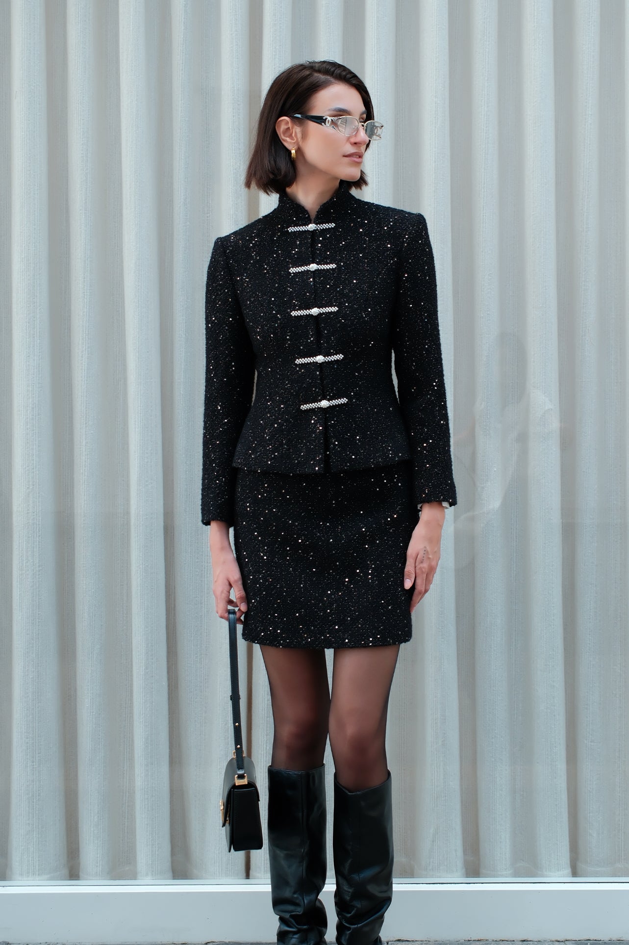 A detailed shot of a woman modeling a sophisticated black woven tweed mini skirt adorned with subtle shimmering crystals, tailored in a sleek high-waisted pencil cut.