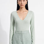 A style comparison of two elegant women's long-sleeve deep V-neck tops featuring subtle rhinestone crystal embellishments; shown on the left in nude camel tucked into tailored trousers, and on the right in pale mint green styled with a white skirt.