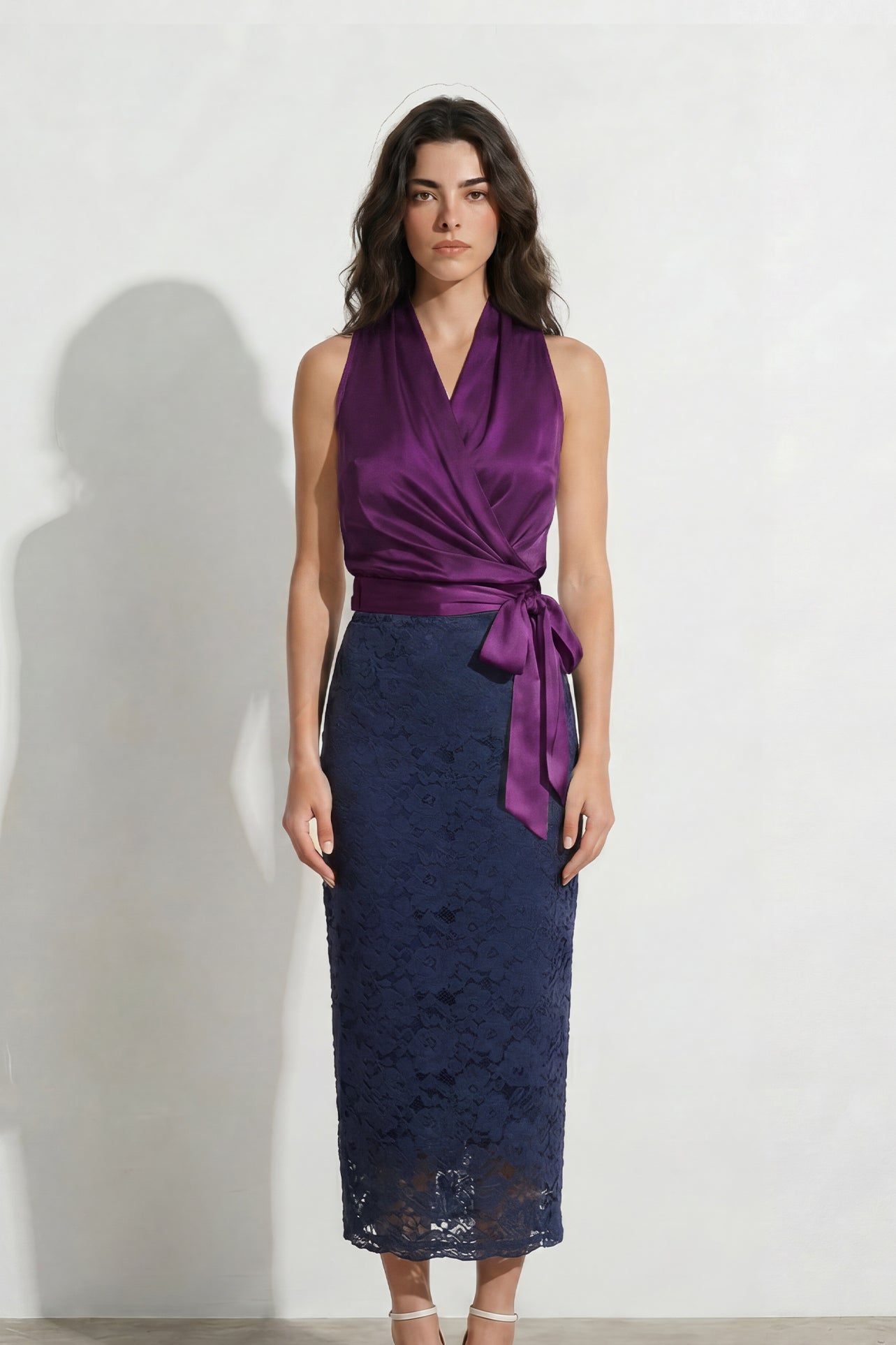 A professional woman modeling an elegant color-block lace sheath dress, featuring a sleeveless white lace bodice with a 3D flower applique on a bateau neckline and a tailored navy blue lace pencil skirt.