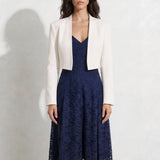A professional woman modeling an elegant navy blue lace midi dress, featuring delicate V-neck spaghetti straps, a tailored fit-and-flare silhouette, and a beautiful flowing asymmetric handkerchief lace trim hem.