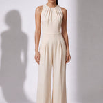 A style comparison of two elegant wide-leg jumpsuits; the left showcasing a sophisticated emerald green tailored pantsuit with a structured crop capelet sleeve, and the right featuring a minimalist cream white sleeveless jumpsuit with refined neck pleating details.