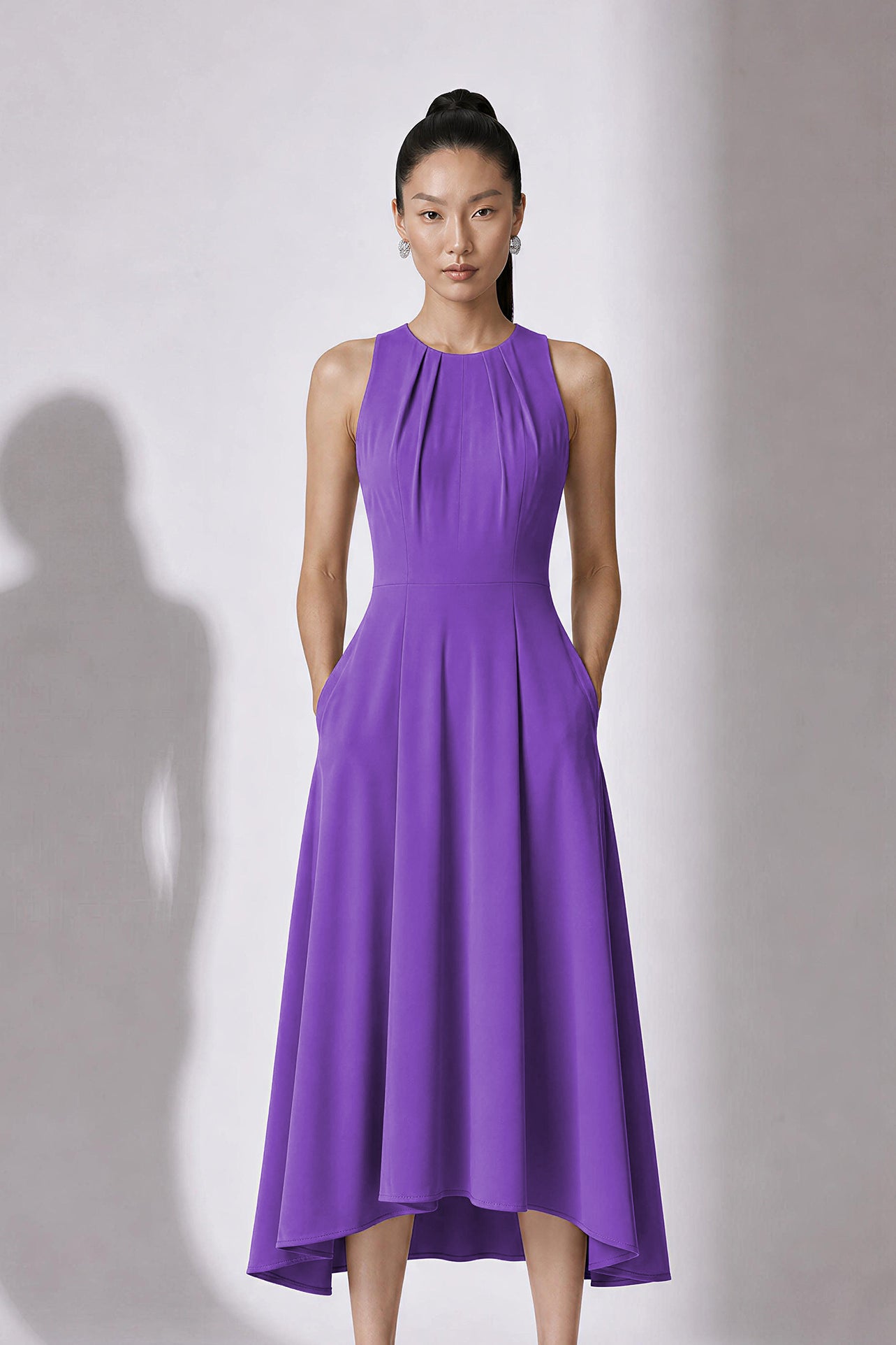 A style comparison of two elegant tailored midi dresses with a flowing high-low hem; the left showcasing a sophisticated light grey dress with a structured collared capelet sleeve, and the right featuring a vibrant purple sleeveless dress with refined pleated neckline and side pockets.