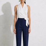 A model showcasing elegant navy blue high-waisted work trousers, featuring a unique curved overlay panel design at the waist, a slim golden metal bar buckle, pressed front creases, and chic cuffed hems, paired with a light blue button-up shirt.