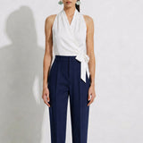 A model showcasing elegant navy blue high-waisted work trousers, featuring a unique curved overlay panel design at the waist, a slim golden metal bar buckle, pressed front creases, and chic cuffed hems, paired with a light blue button-up shirt.