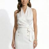 A professional woman modeling elegant satin halter wrap tops in crisp white and deep purple, featuring a sophisticated side bow tie and paired with white high-waisted trousers and a button-front skirt.