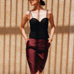 A style comparison of two elegant women's high-waisted pencil skirts featuring an overlapping crossover tulip hemline; shown on the left in deep navy blue paired with a white shirt, and on the right in rich burgundy wine paired with a matching long-sleeve top and suede clutch.