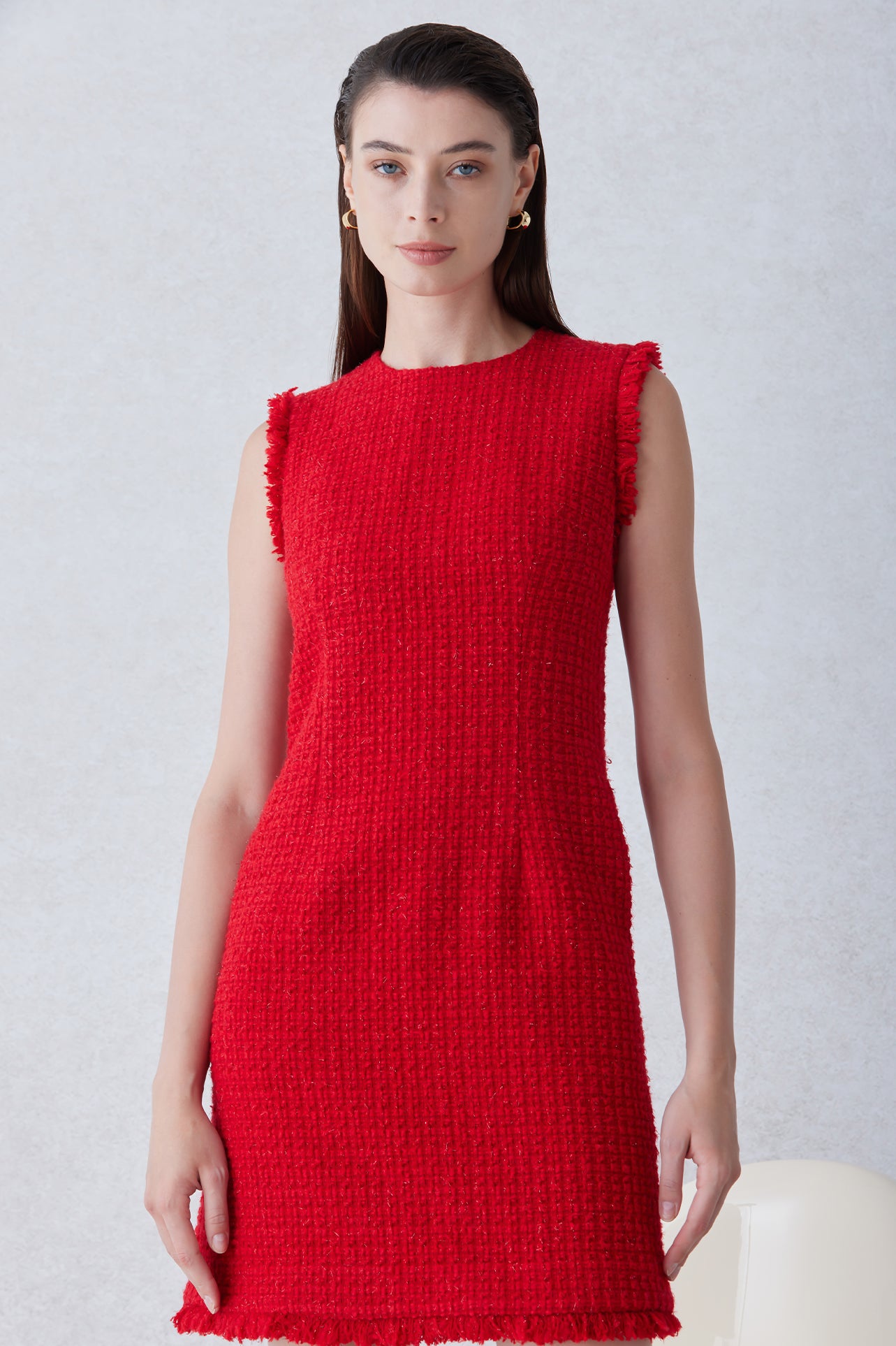 A professional woman wearing a sophisticated vibrant red tweed sleeveless mini dress, featuring a classic round neck, elegant frayed edges, and a slimming black waist belt for a chic holiday or office look.