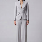 A professional woman wearing a sophisticated light grey tailored suit set, featuring a unique wrap-front blazer with criss-cross waist detailing and matching slim-fit trousers for a polished executive look.