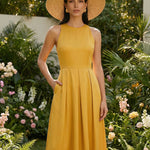 Two professional models wearing elegant halter-neck pleated maxi dresses in khaki and mustard yellow, featuring a high-waist A-line silhouette and side pockets, perfect for a sophisticated summer vacation or garden party look.