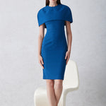 A professional woman wearing a sophisticated teal blue midi dress with an elegant cape-style overlay and structured shoulders, perfect for formal executive events and ceremonial occasions.