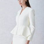 A professional woman wearing a sophisticated cream tweed skirt suit, featuring a tailored jacket with a modern front zipper and an elegant stand collar for a polished executive office look.