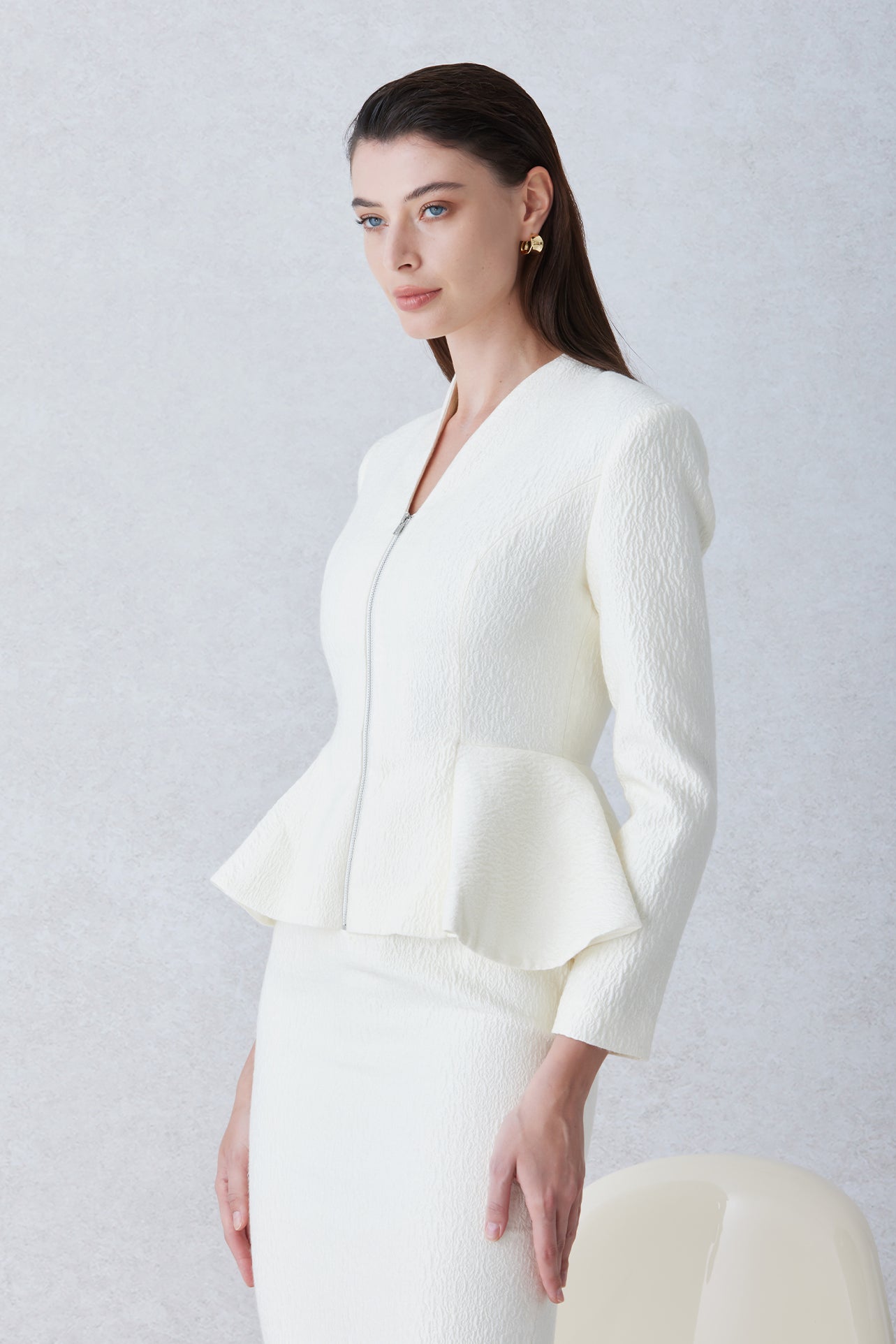 A professional woman wearing a sophisticated cream tweed skirt suit, featuring a tailored jacket with a modern front zipper and an elegant stand collar for a polished executive office look.