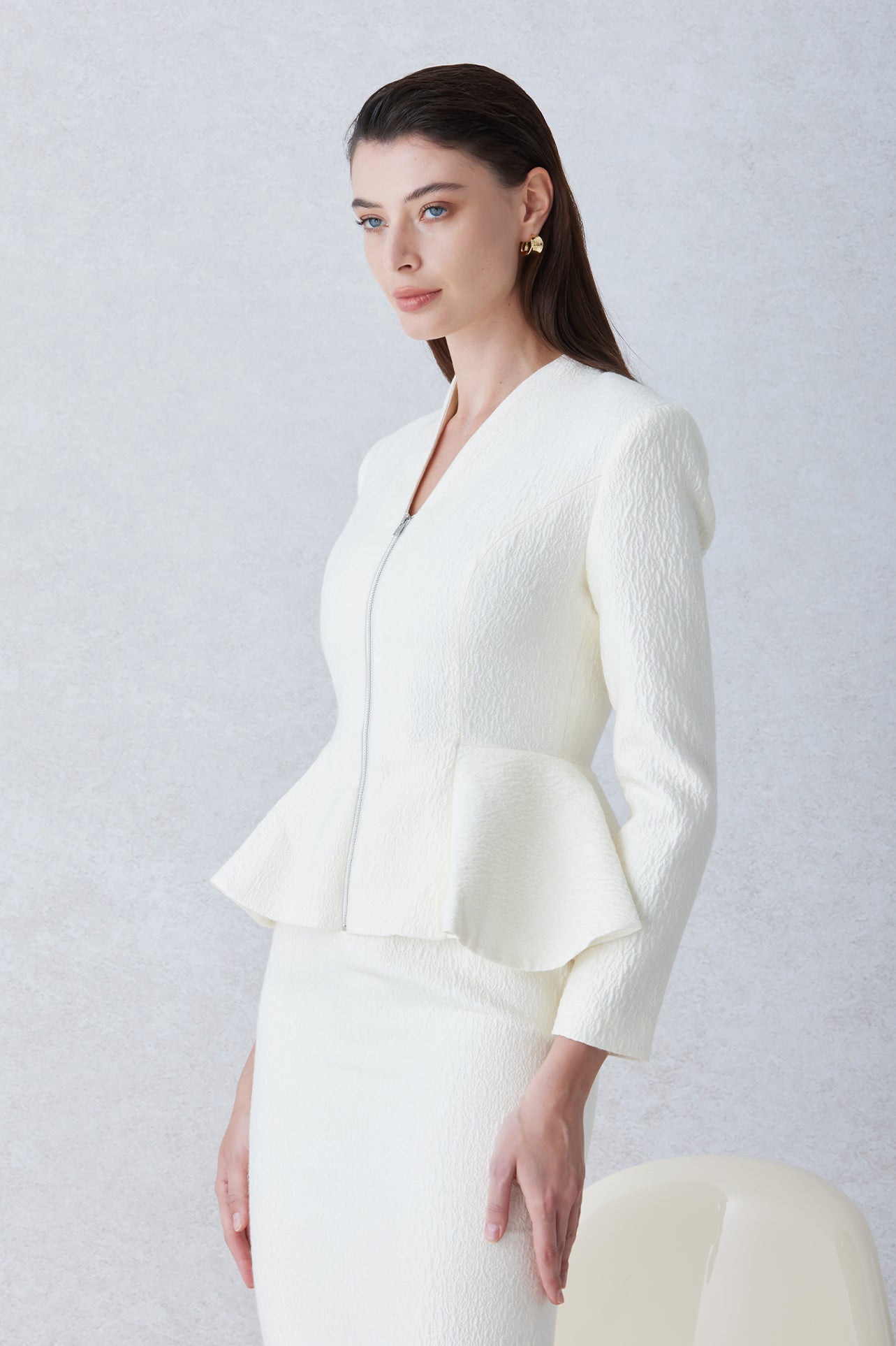 A professional woman wearing a sophisticated cream tweed skirt suit, featuring a tailored jacket with a modern front zipper and an elegant stand collar for a polished executive office look.