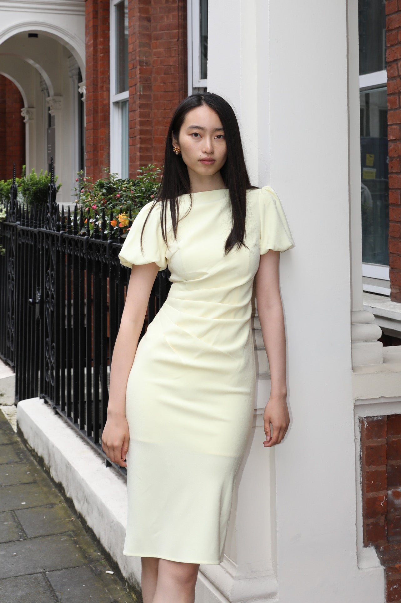 A professional woman wearing a sophisticated pale yellow short-sleeve midi dress, featuring elegant puff sleeves and a slimming ruched waistline for a polished and fresh summer office look.