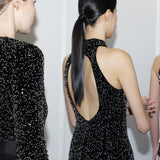 A stunning woman wearing a sophisticated black sequin halter midi dress, featuring a traditional mandarin collar and a shimmering bodycon silhouette, perfect for a modern oriental-inspired evening party look.