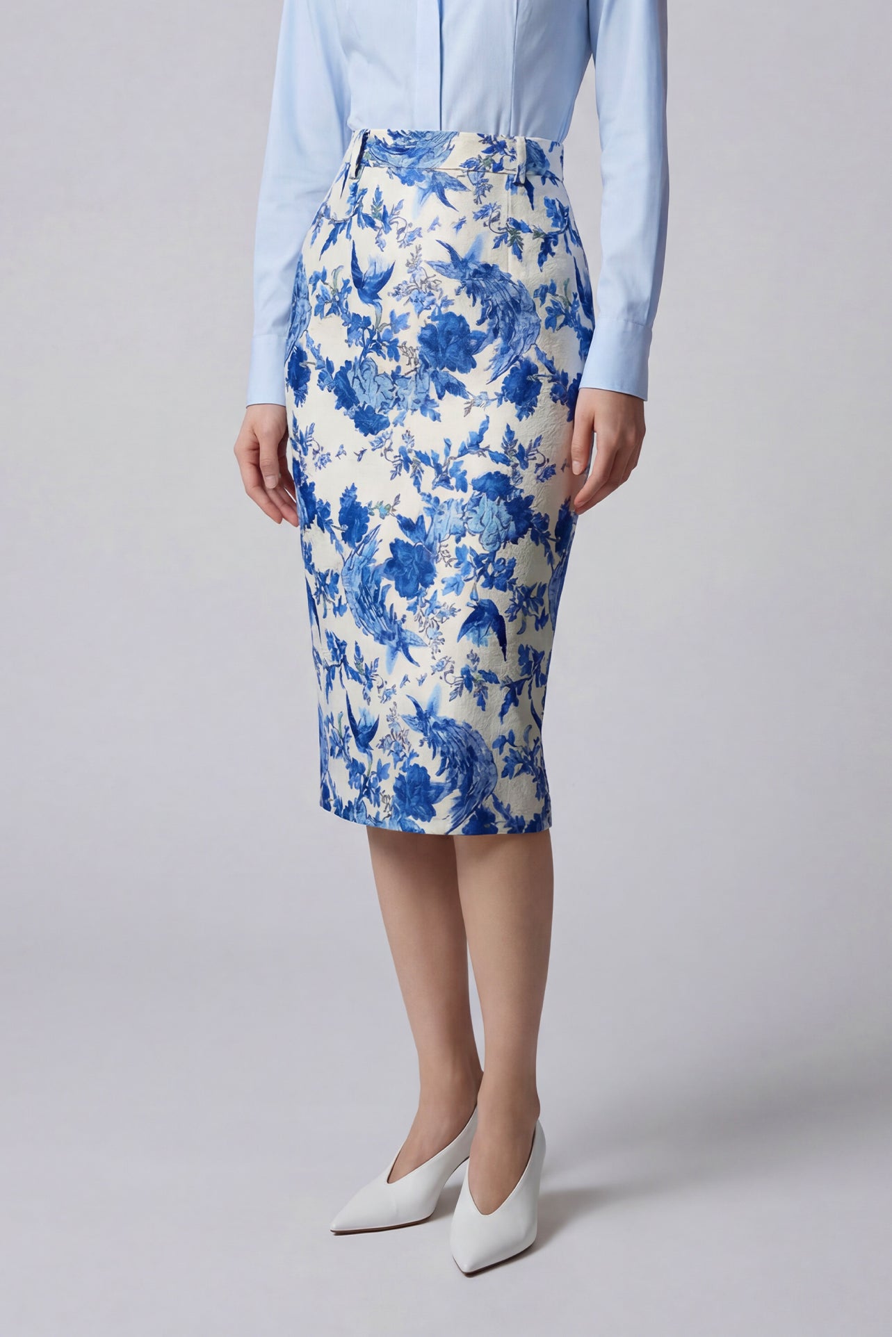 An elegant professional woman wearing a high-waisted pencil skirt featuring a sophisticated blue and white floral porcelain-style print, perfect for a polished office look.