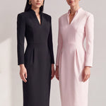 A style comparison of two elegant women modeling tailored long-sleeve midi dresses featuring a sophisticated stand collar with a split V-neckline and flattering double waist pleats; shown on the left in classic black and on the right in soft blush pink.