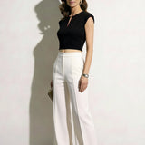 A professional woman modeling an elegant black and white color-block sheath dress, featuring a sleeveless black bodice with metallic hardware and a tailored white pencil skirt for a sophisticated executive look.