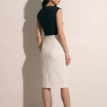 A professional woman modeling an elegant black and white color-block sheath dress, featuring a sleeveless black bodice with metallic hardware and a tailored white pencil skirt for a sophisticated executive look.
