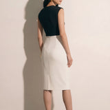 A professional woman modeling an elegant black and white color-block sheath dress, featuring a sleeveless black bodice with metallic hardware and a tailored white pencil skirt for a sophisticated executive look.