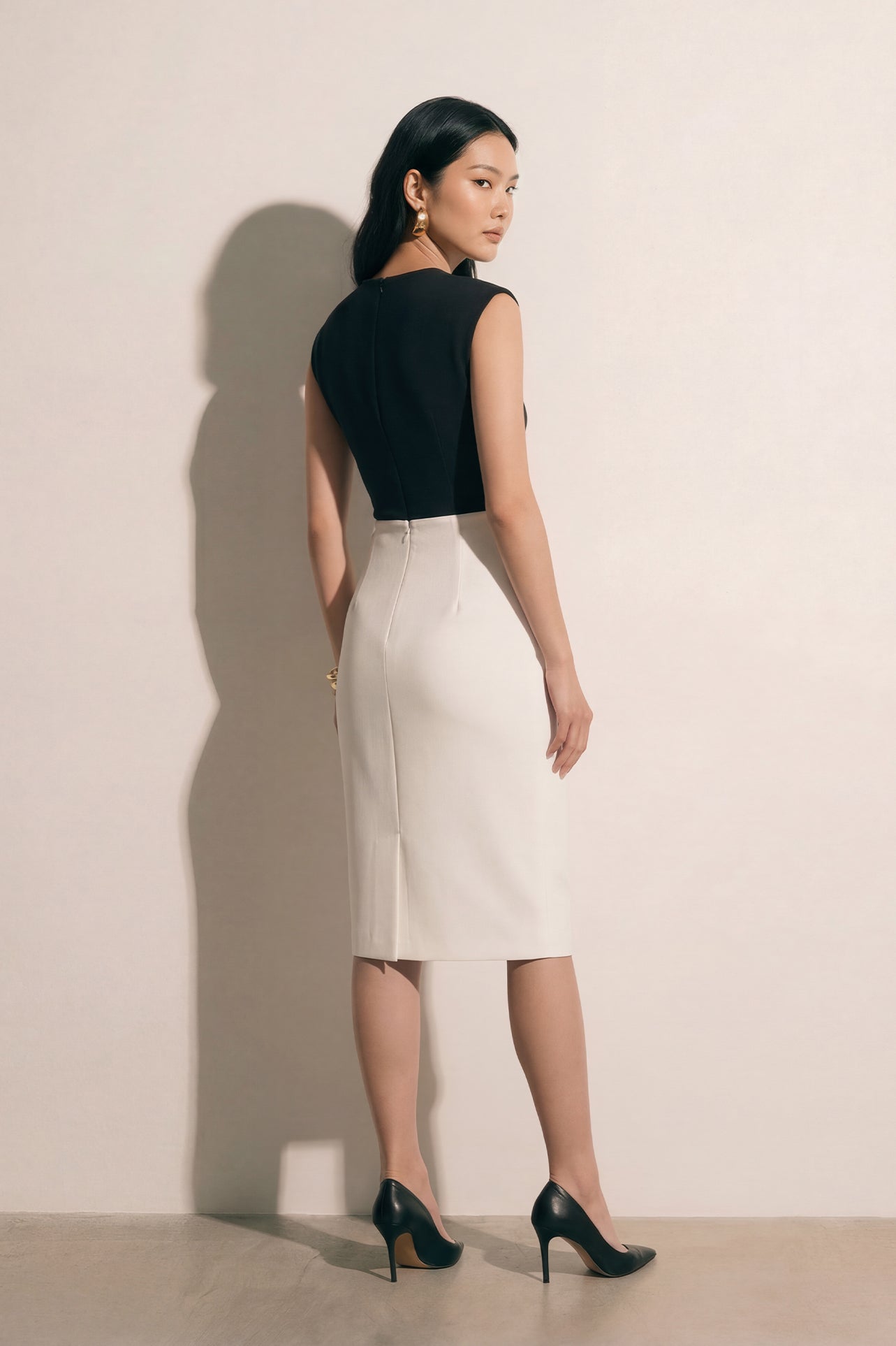 A professional woman modeling an elegant black and white color-block sheath dress, featuring a sleeveless black bodice with metallic hardware and a tailored white pencil skirt for a sophisticated executive look.