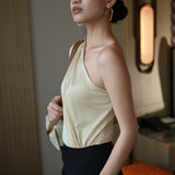 A stylish Asian woman modeling a sophisticated cream-colored asymmetric one-shoulder top featuring a single long sleeve, elegant diagonal draped pleats, and styled with high-waisted black trousers.