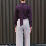 A chic woman wearing an elegant deep plum long-sleeve blouse with an asymmetric high-neck scarf tie, neatly tucked into a high-waisted black tweed skirt embellished with subtle sparkling sequins.