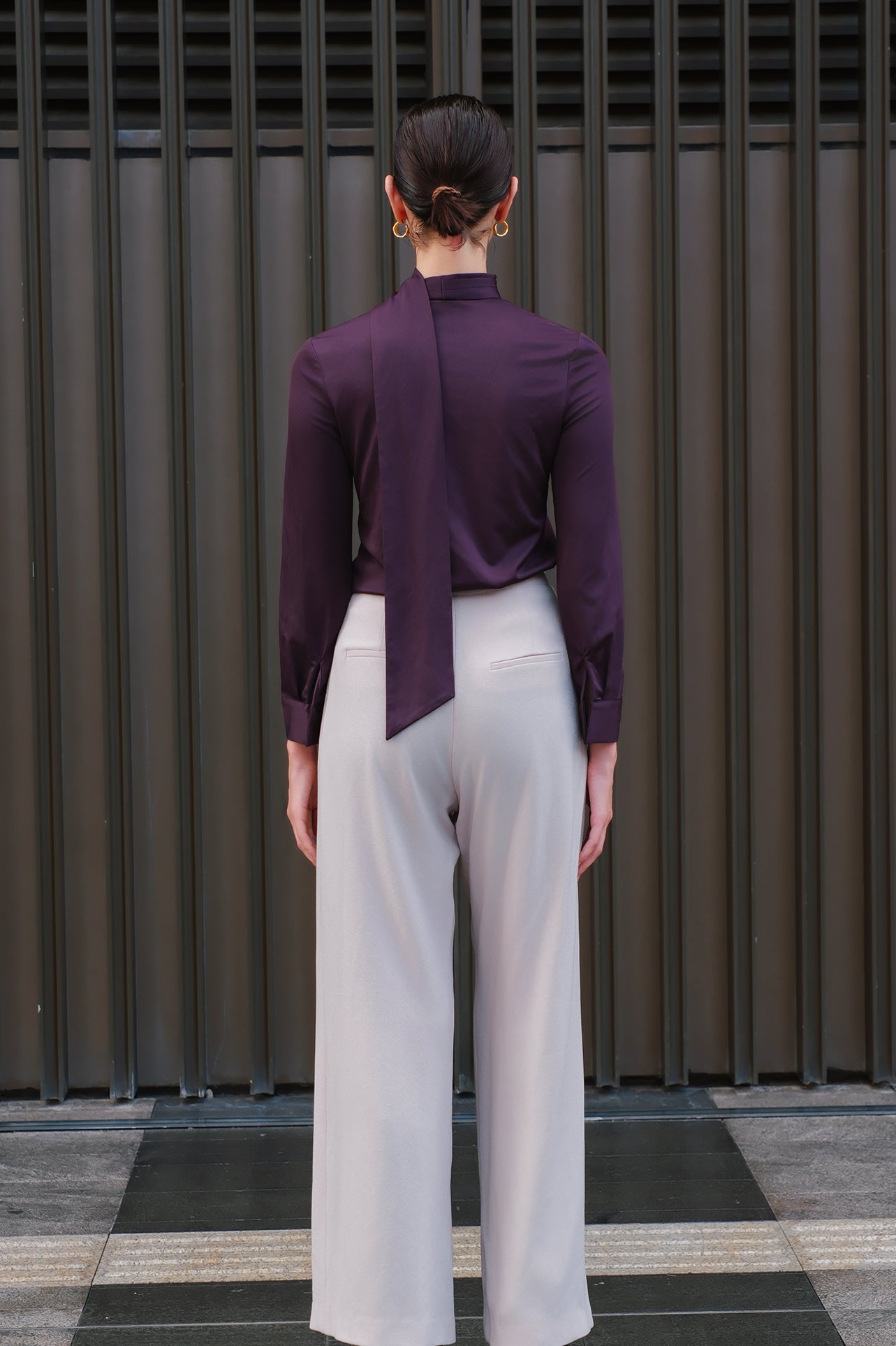 A chic woman wearing an elegant deep plum long-sleeve blouse with an asymmetric high-neck scarf tie, neatly tucked into a high-waisted black tweed skirt embellished with subtle sparkling sequins.