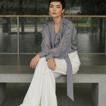 A style comparison of two professional office outfits featuring high-waisted white wide-leg trousers; the left paired with a vibrant purple ruffled V-neck chiffon blouse, and the right styled with a sophisticated grey long-sleeve blouse with a flowing tie-neck scarf.