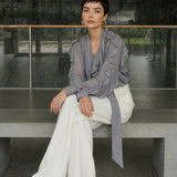 A style comparison of two professional office outfits featuring high-waisted white wide-leg trousers; the left paired with a vibrant purple ruffled V-neck chiffon blouse, and the right styled with a sophisticated grey long-sleeve blouse with a flowing tie-neck scarf.