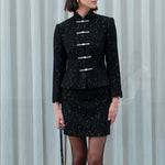 A chic woman wearing a luxurious black sparkle tweed tailored jacket featuring an authentic stand cheongsam collar, elegant horizontal pearl bar closures, and a flattering hourglass waistline.