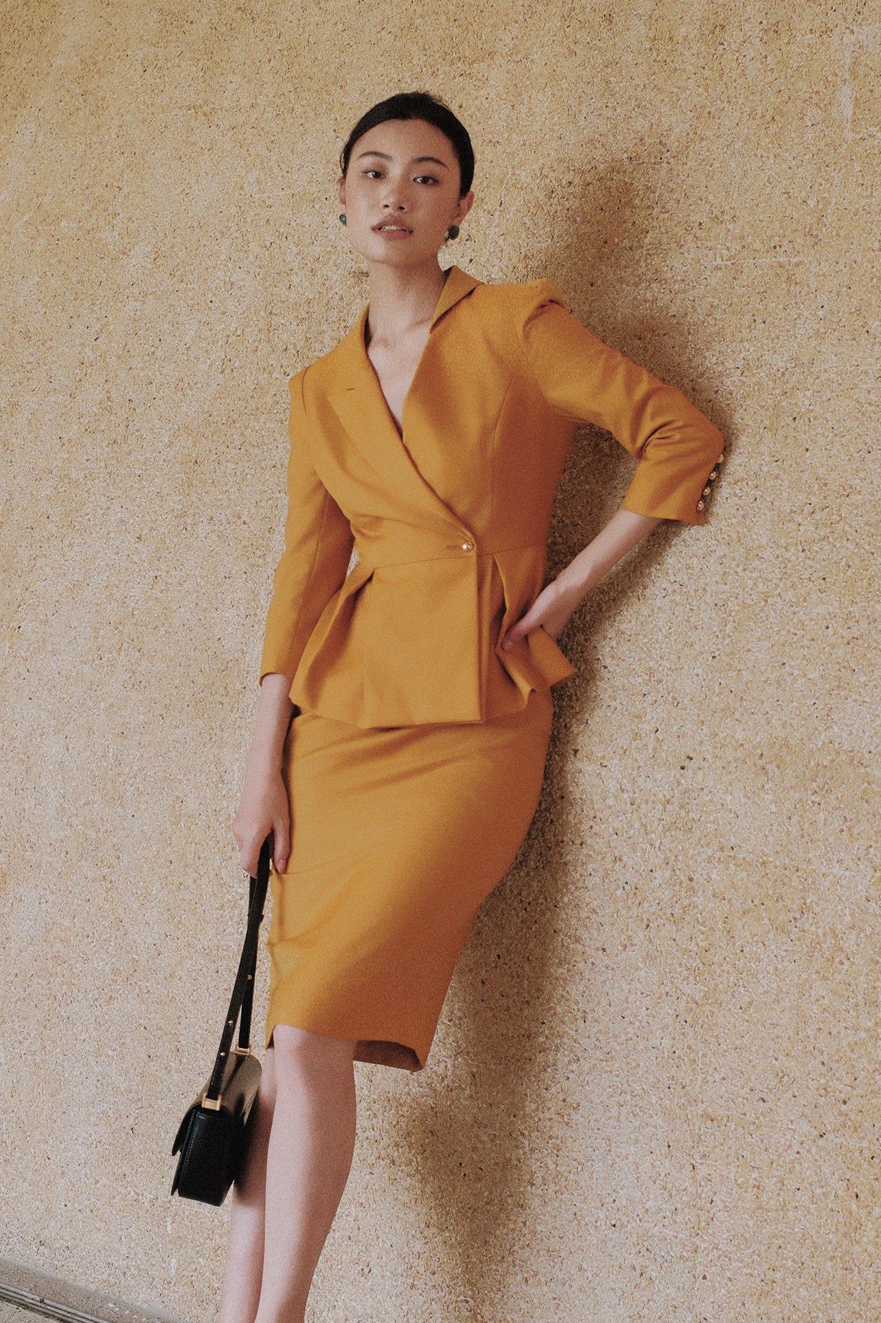 A style comparison of two elegant women's skirt suit sets featuring three-quarter sleeve blazers with single-button closure and pleated peplum hems, paired with matching pencil skirts in mustard yellow and deep teal blue.