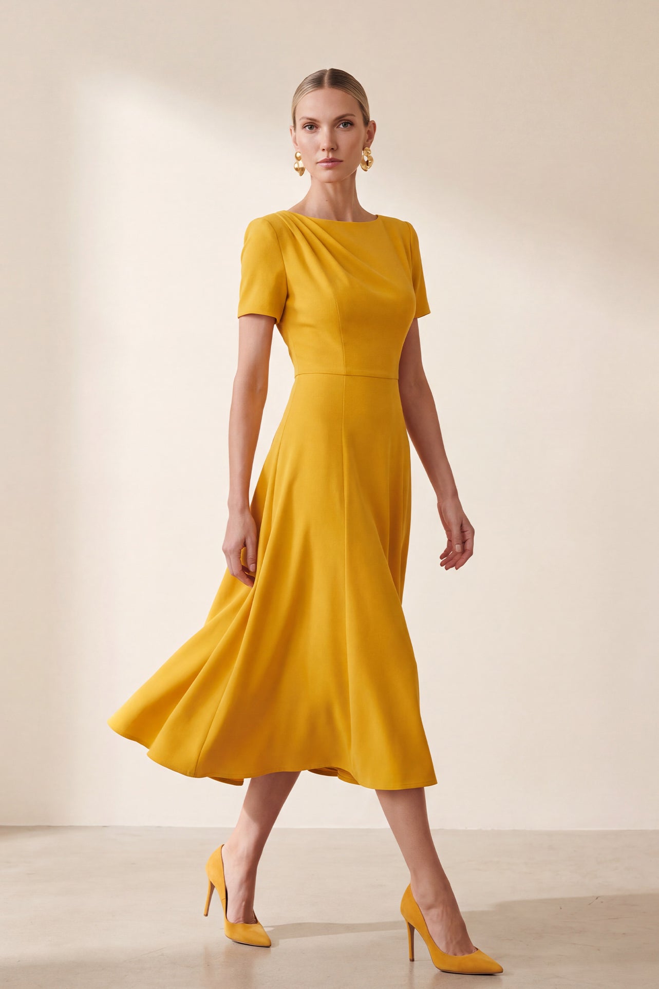 A blonde model wearing a sophisticated mustard yellow A-line midi dress featuring an elegant boat neckline with subtle shoulder pleating, short sleeves, and a flattering flared skirt.