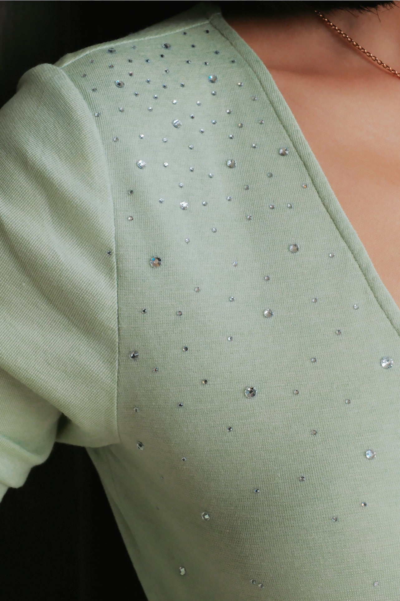 A style comparison of two elegant women's long-sleeve deep V-neck tops featuring subtle rhinestone crystal embellishments; shown on the left in nude camel tucked into tailored trousers, and on the right in pale mint green styled with a white skirt.