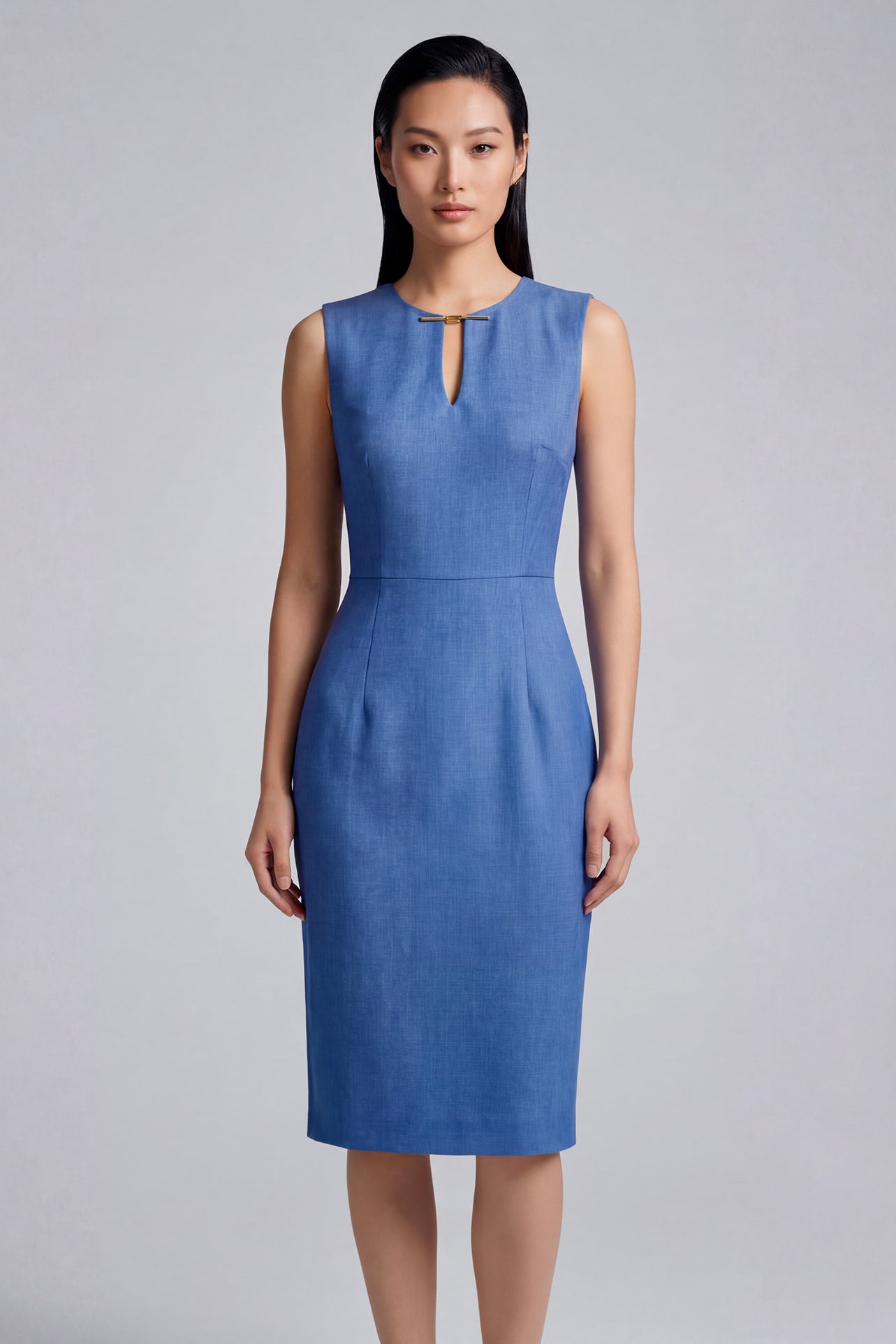 A professional woman modeling an elegant slate blue sleeveless sheath dress, featuring a sophisticated keyhole neckline with a delicate gold metal hardware detail and a tailored slim fit for corporate office wear.