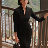 A style comparison of two elegant women modeling tailored long-sleeve midi dresses featuring a sophisticated stand collar with a split V-neckline and flattering double waist pleats; shown on the left in classic black and on the right in soft blush pink.