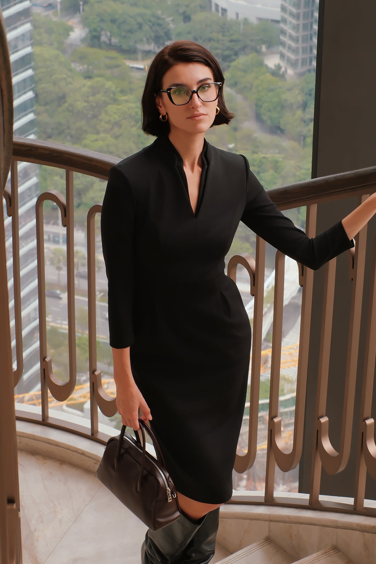 A style comparison of two elegant women modeling tailored long-sleeve midi dresses featuring a sophisticated stand collar with a split V-neckline and flattering double waist pleats; shown on the left in classic black and on the right in soft blush pink.