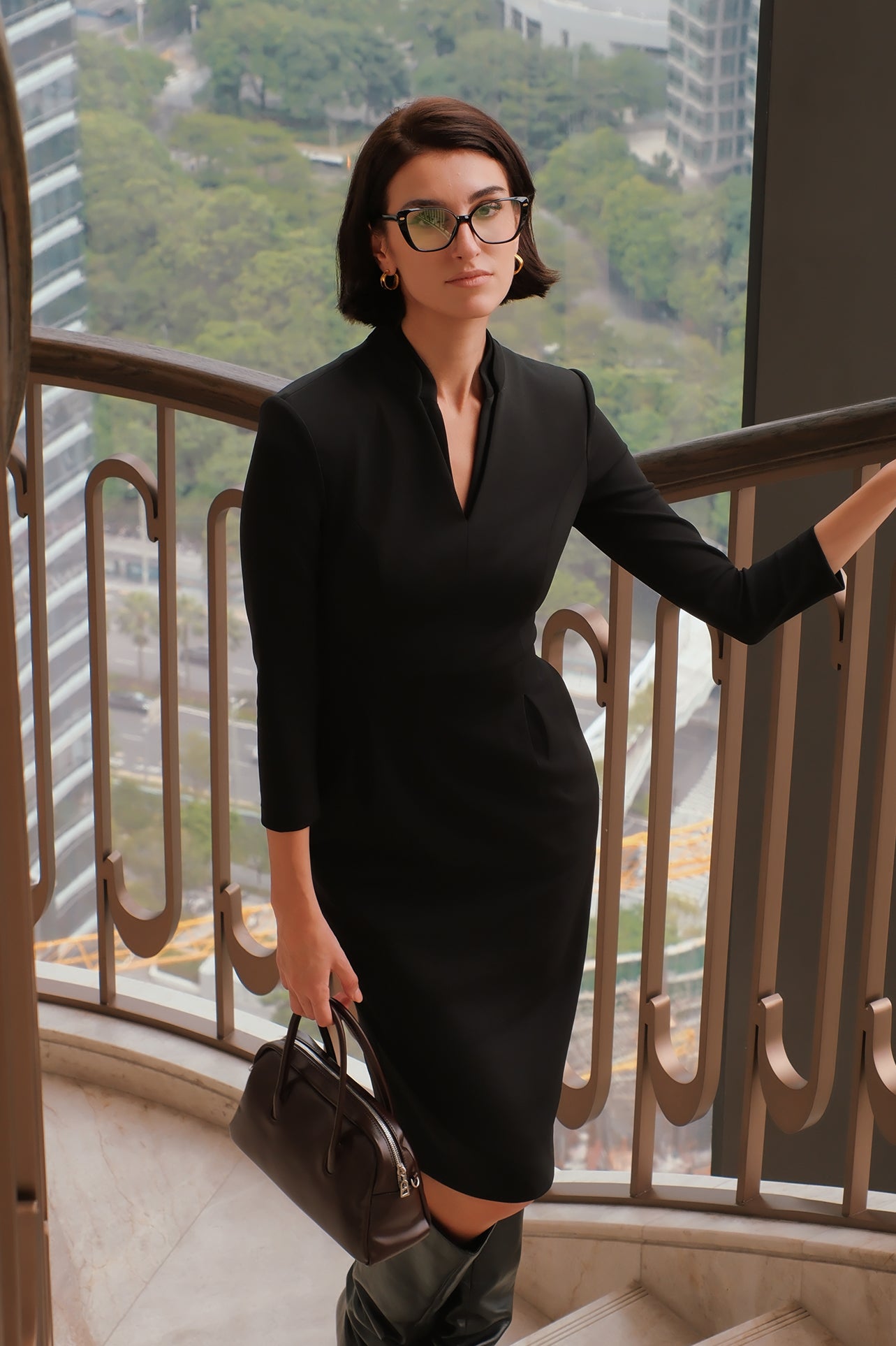 A style comparison of two elegant women modeling tailored long-sleeve midi dresses featuring a sophisticated stand collar with a split V-neckline and flattering double waist pleats; shown on the left in classic black and on the right in soft blush pink.