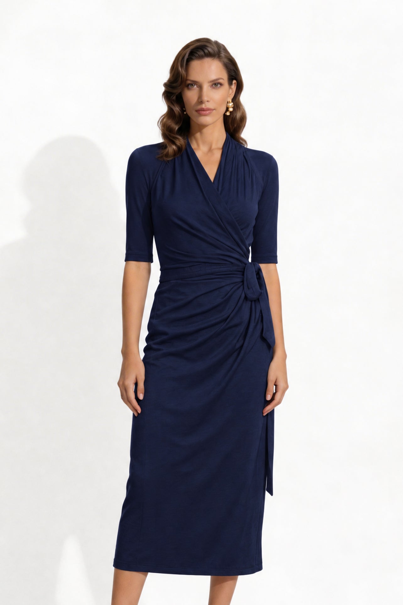 Two professional models wearing elegant wrap midi dresses with elbow-length sleeves; the left in a soft pastel lavender and the right in a deep navy blue, both featuring a sophisticated surplice V-neckline and slimming side ruched draping with a waist tie.