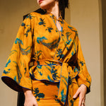 A beautiful woman modeling an elegant mustard yellow modern Chinese jacket, featuring intricate blue phoenix embroidery, a sophisticated mandarin collar, and wide kimono sleeves with a matching waist tie.