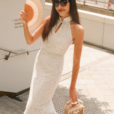 A professional woman modeling an elegant white lace halter neck modern qipao dress, featuring a sophisticated mandarin collar with keyhole detail and an intricate eyelet embroidered fabric for a quiet luxury look.