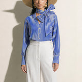 A style collection of three models presenting elegant dopamine office wear; the left in a white bow-tie blouse with a mustard yellow front-slit midi skirt, the center wearing a blue striped pussy-bow shirt with a straw hat and white wide-leg trousers, and the right in a vibrant orange satin blouse with a royal blue pencil skirt