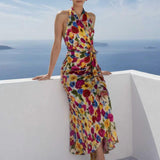 A beautiful professional model presenting an elegant tropical floral print halter maxi dress with a blue ocean background; featuring a sophisticated wrap tie-waist silhouette and vibrant multicolored botanical patterns for a chic summer resort look.