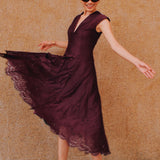 A chic woman wearing sunglasses and an elegant deep burgundy sleeveless V-neck A-line midi dress featuring textured jacquard fabric, delicate lace hemline, and a matching flowing neck scarf.