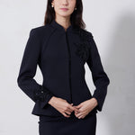 A professional woman wearing a sophisticated black skirt suit, featuring a mandarin collar with elegant leaf embroidery on the shoulder and skirt, and traditional frog button detailing for a modern oriental executive look.
